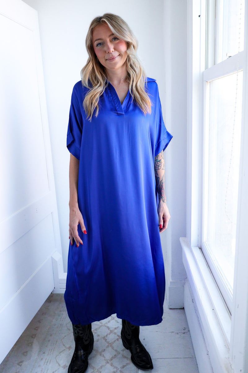Woman wearing a blue dress standing in a bright room with large windows.