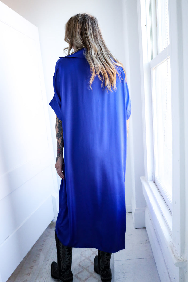 Person wearing a long blue dress in a bright room with white walls and a window.