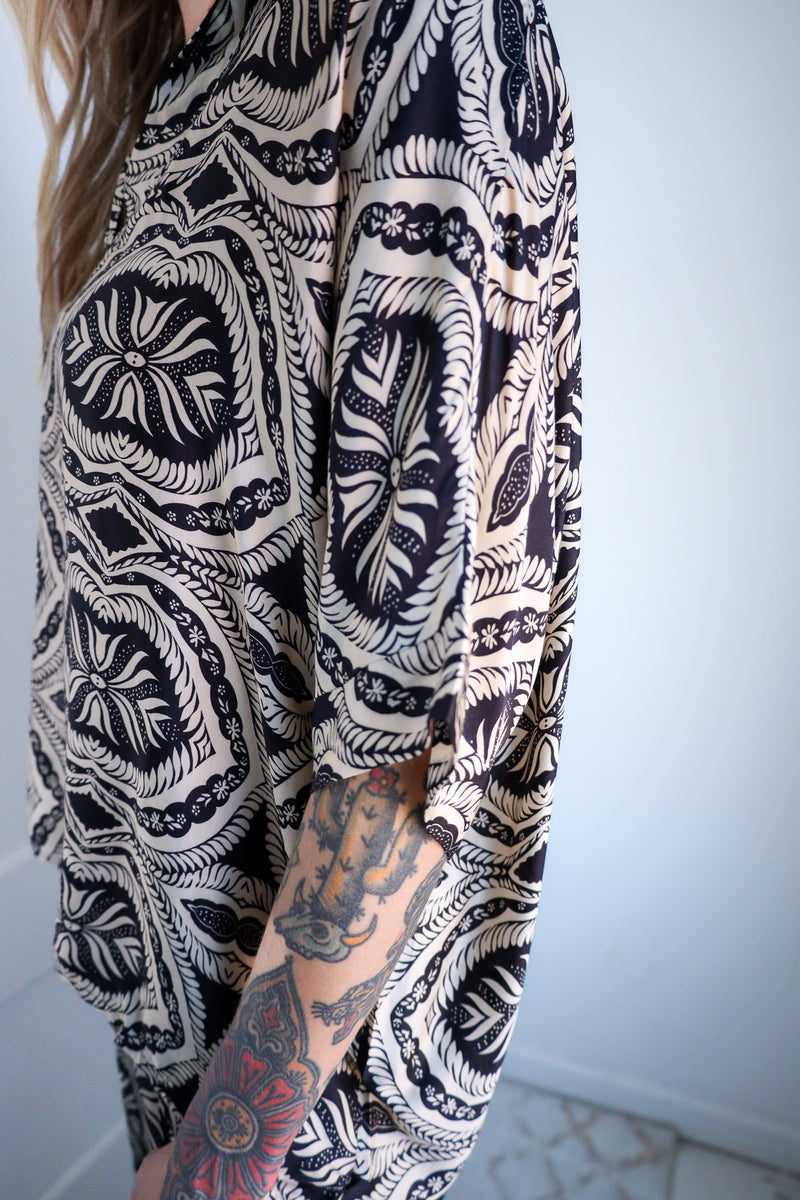 Person wearing a black and white patterned outfit with tattoos visible on arms.