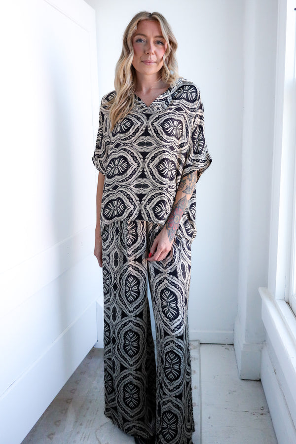 Woman wearing a patterned outfit standing in a bright room with white walls and floor.