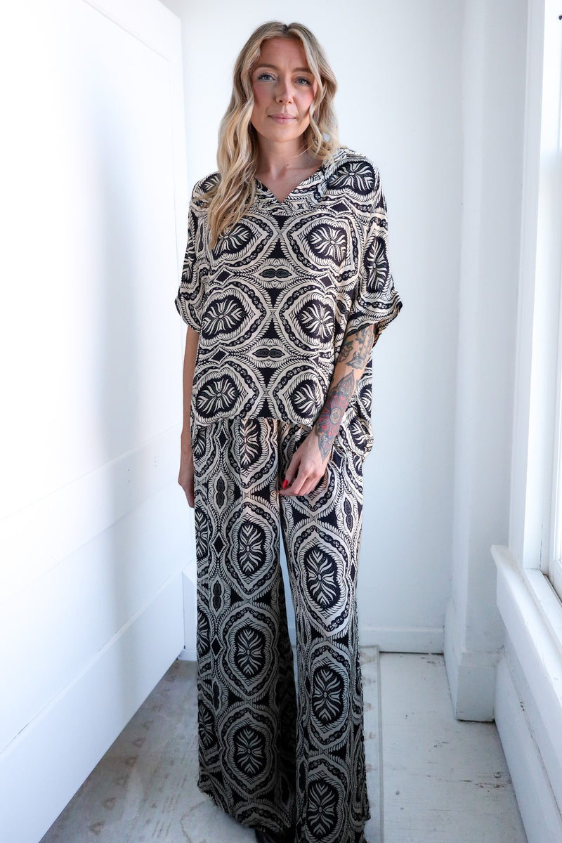 Woman wearing a patterned outfit standing in a bright room with white walls and floor.