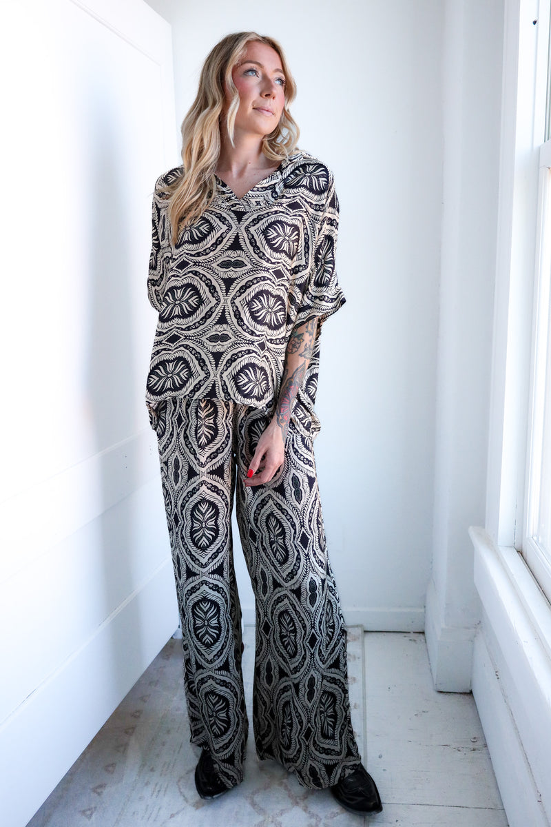 Woman wearing a patterned outfit standing in a bright room with white walls and floor.