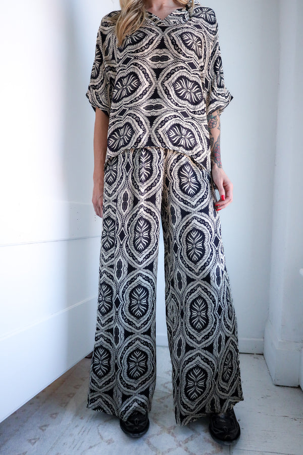 Person wearing a patterned jumpsuit standing against a white wall.