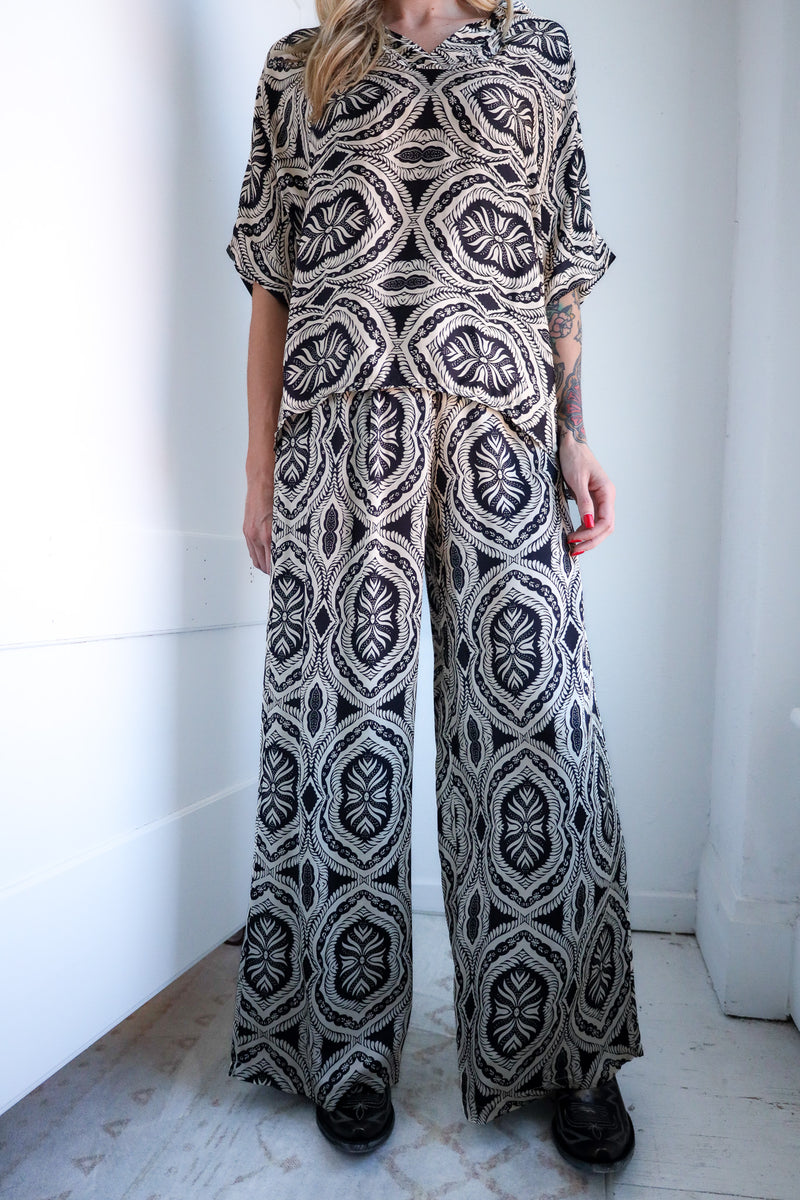 Person wearing a patterned jumpsuit standing against a white wall.