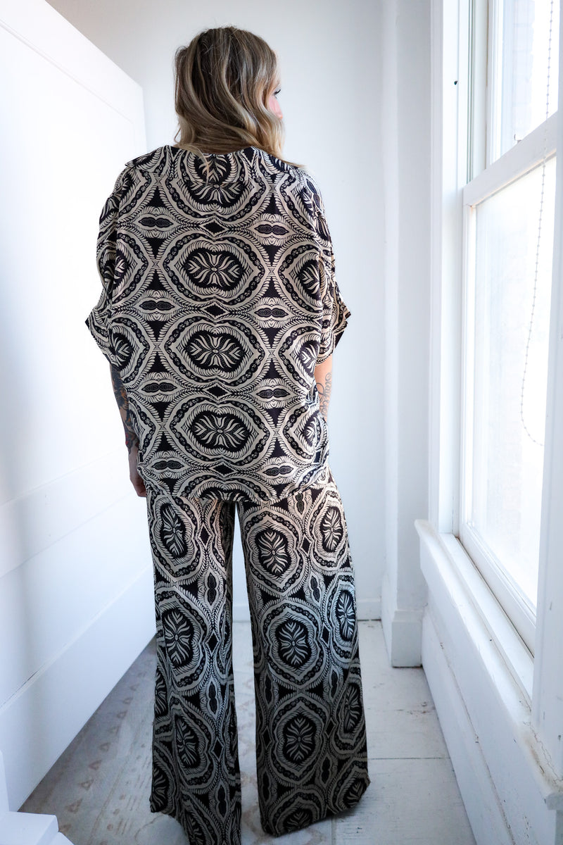 Person wearing a black and white patterned outfit standing in a bright room with large windows.