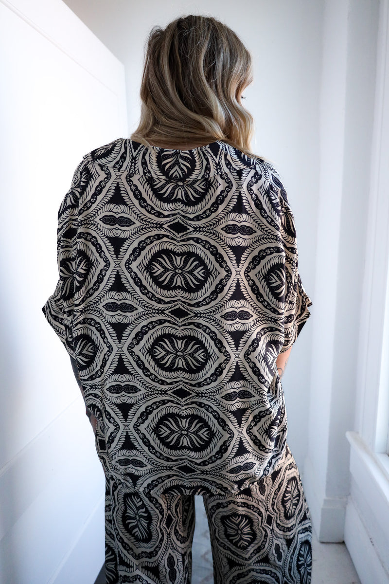 Person wearing a black and white patterned outfit in a minimal white room.