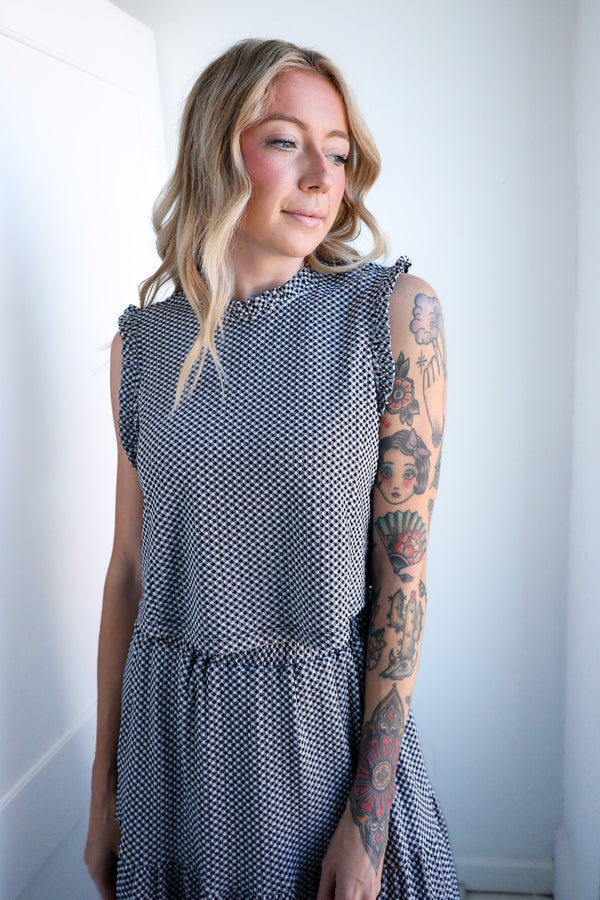 Woman wearing a sleeveless patterned dress against a plain background