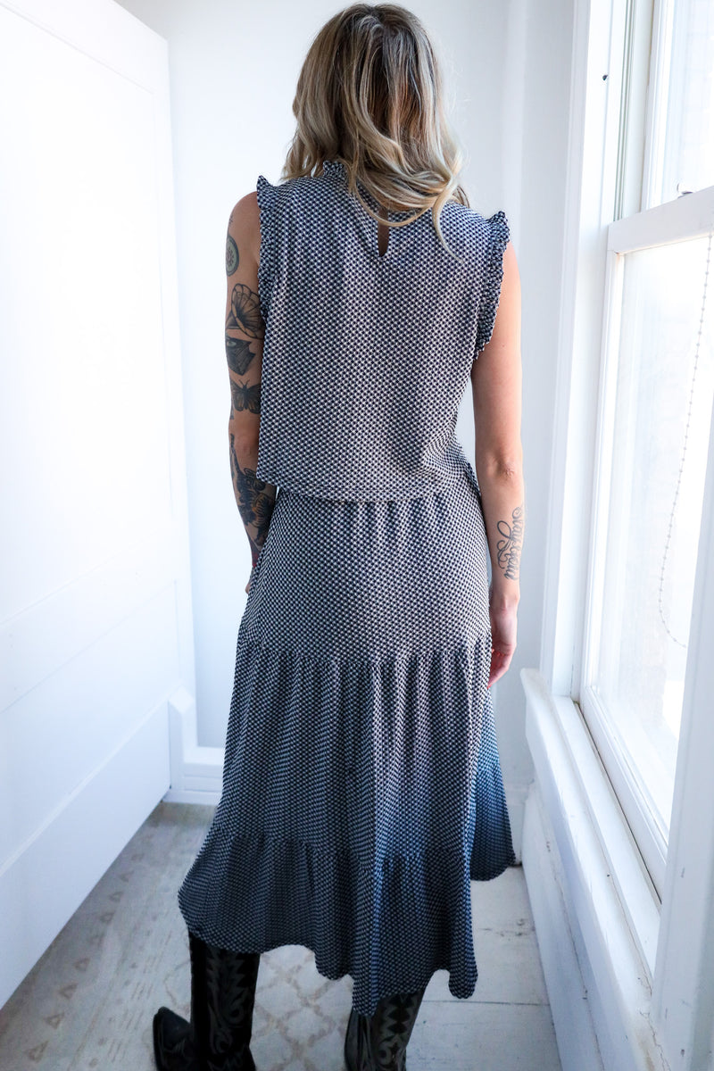Woman wearing a sleeveless, patterned dress standing in a bright room with white walls and a window.