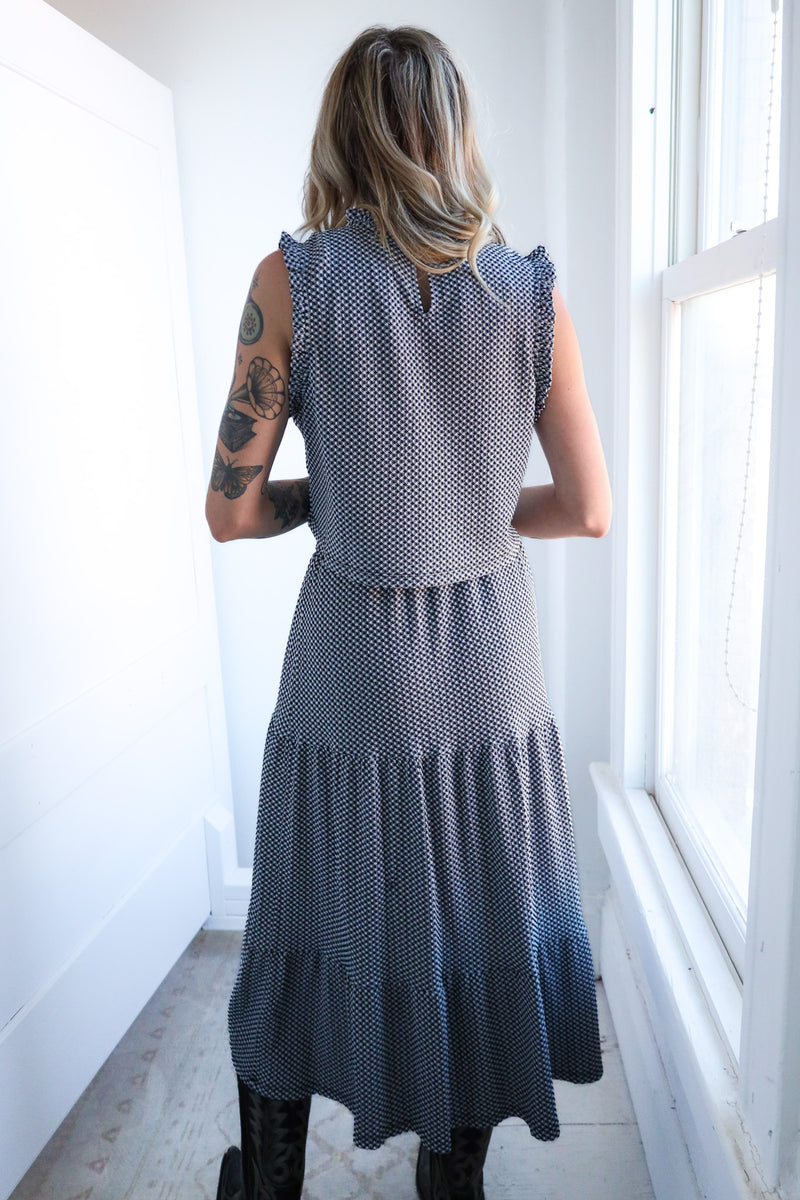 Woman wearing a blue polka dot dress standing in a bright room with white walls and a window.