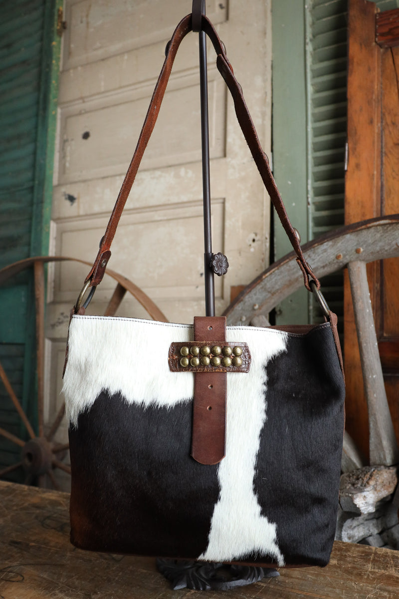 Black and white cowhide handbag with brown leather accents on a wooden surface.