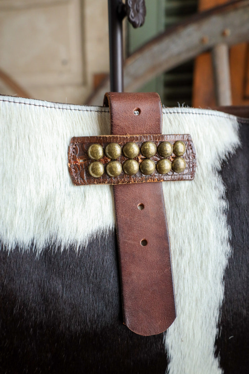 Brown leather strap with gold studs on a black and white cowhide background