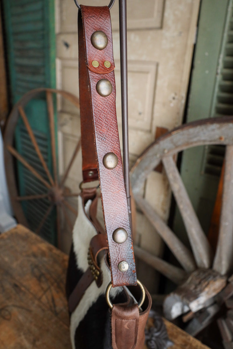 Brown leather strap with metal studs and ring, rustic background