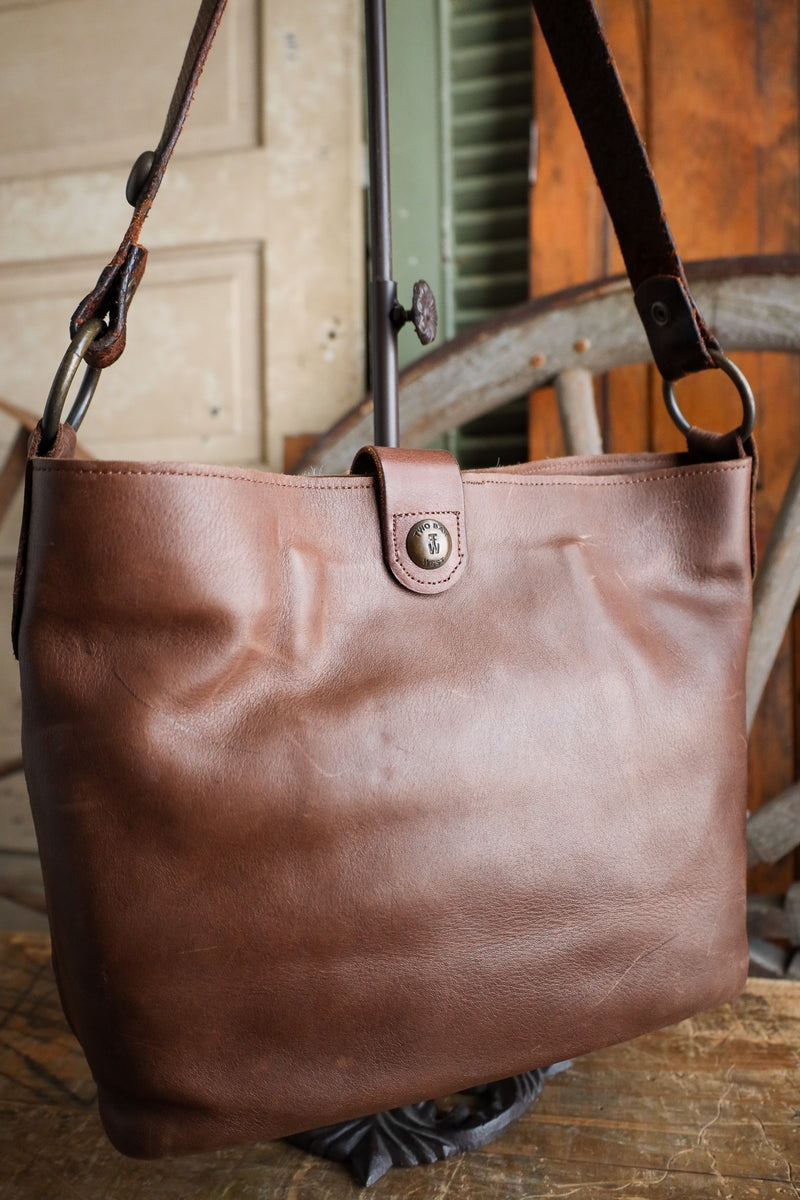 Brown leather tote bag with a strap on a wooden surface