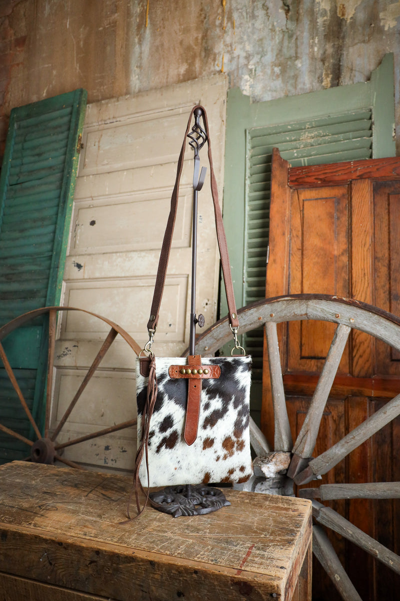 Cow print handbag with brown leather strap on a wooden surface with rustic background