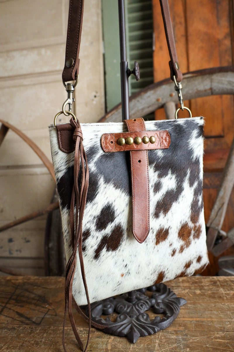 Cowhide leather handbag with brown leather strap on a wooden surface