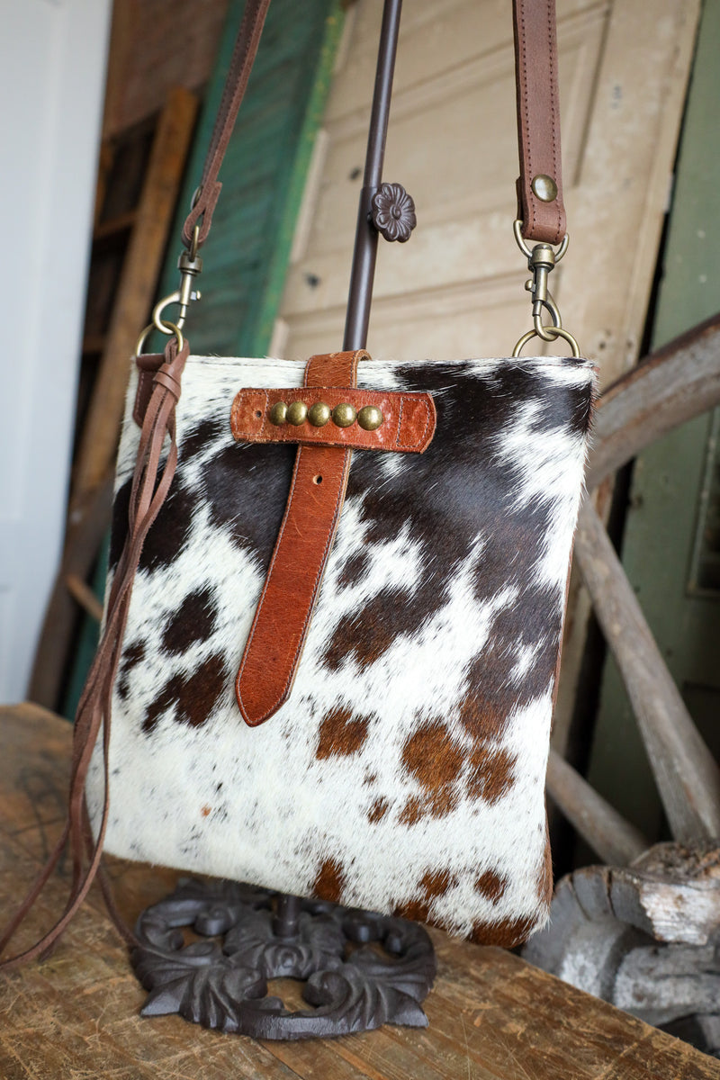 Cow print handbag with brown leather strap on a rustic wooden surface