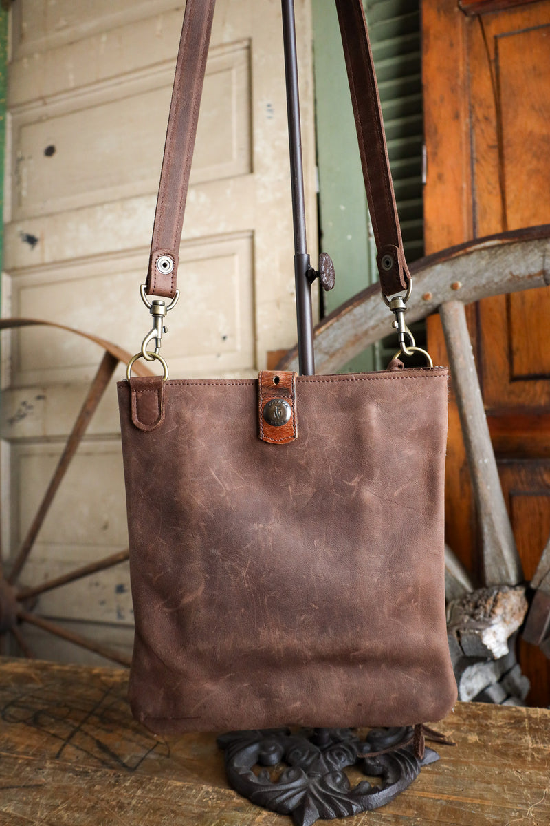 Brown leather tote bag with a strap on a wooden surface