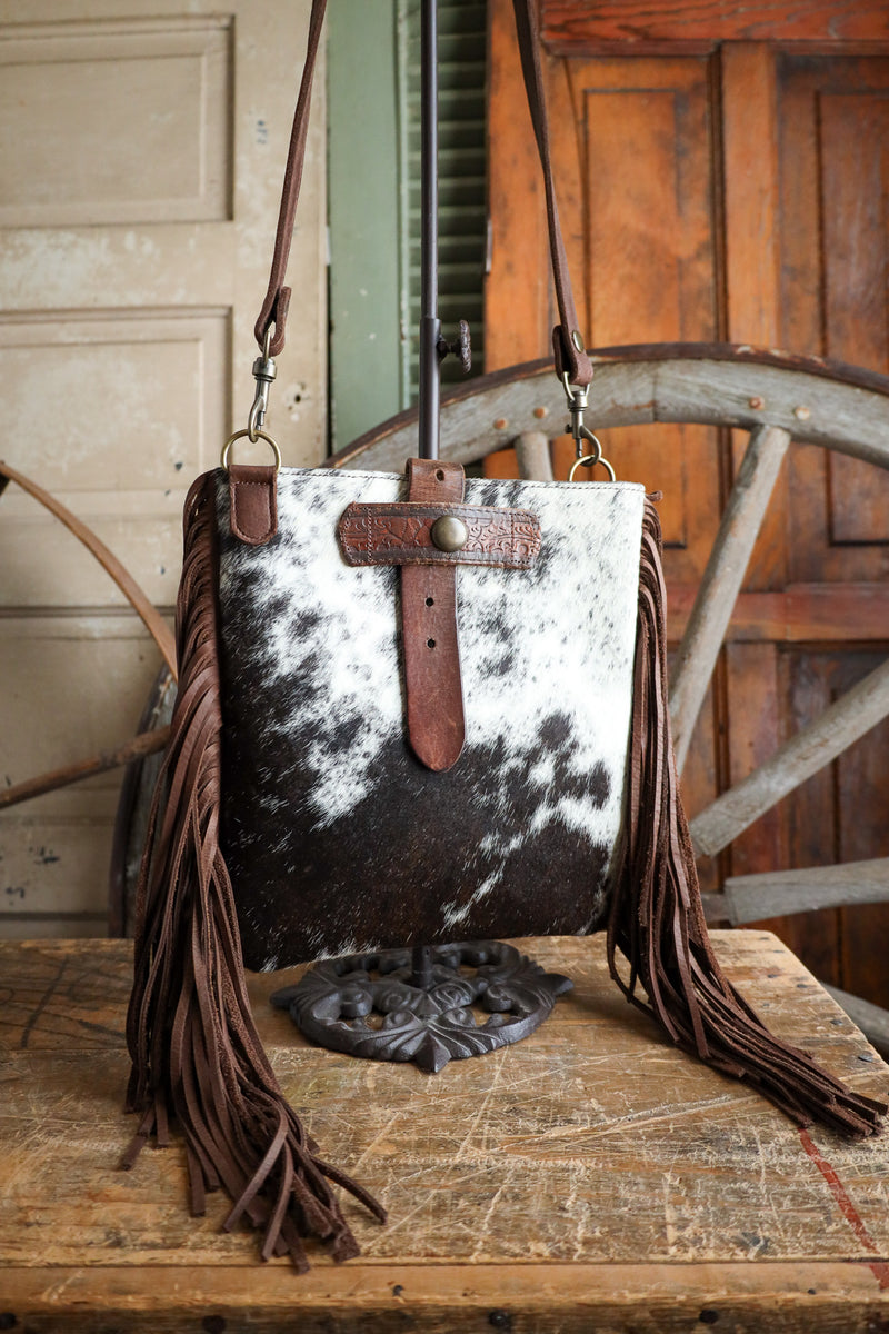 Cowhide leather handbag with fringe on a wooden surface, rustic background