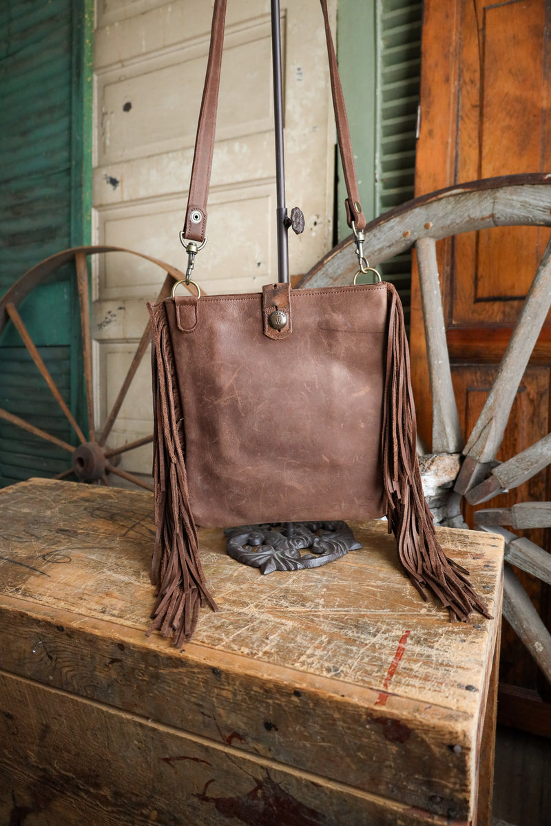 Brown leather handbag with fringes on a wooden surface with rustic background