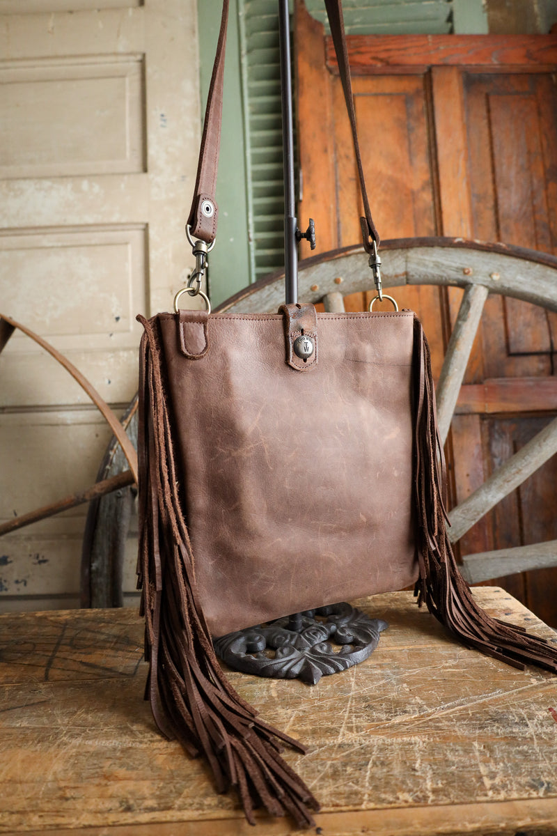Brown leather bag with fringes on a wooden surface with rustic background