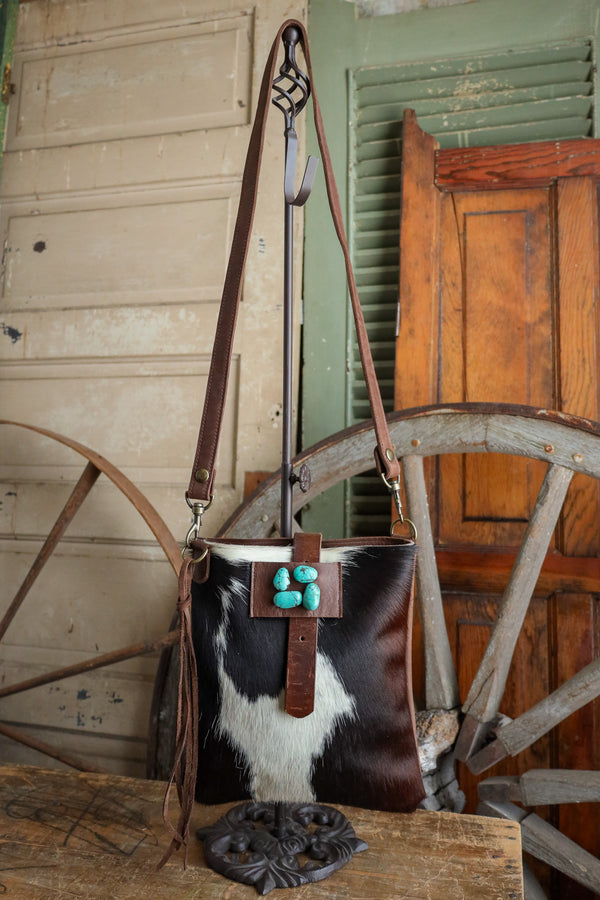 Cowhide handbag with turquoise buttons on a wooden surface with a rustic background