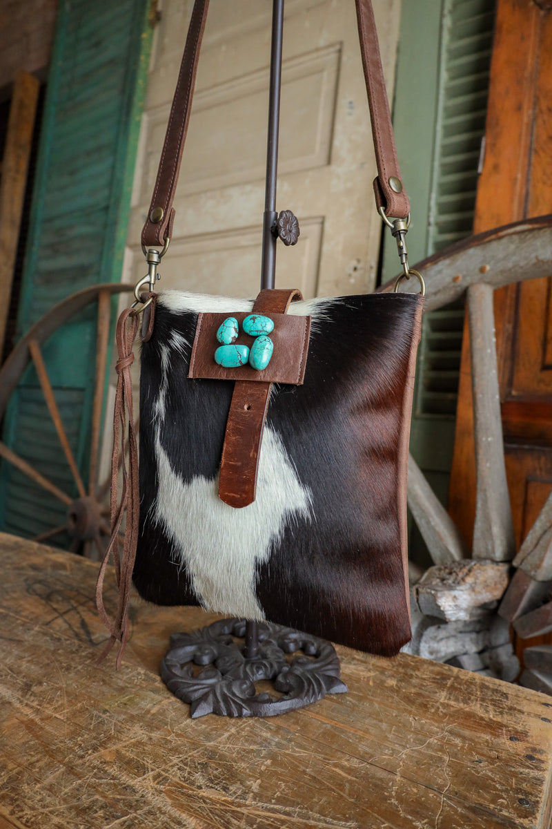 Cowhide leather handbag with turquoise stones on a wooden surface