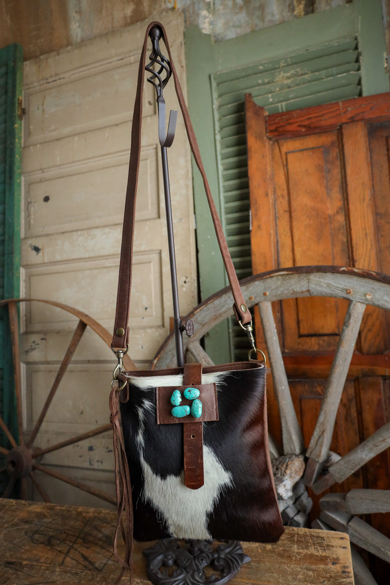 Brown leather bag with turquoise stones on a horse's headstall in front of wooden doors and wagon wheels.