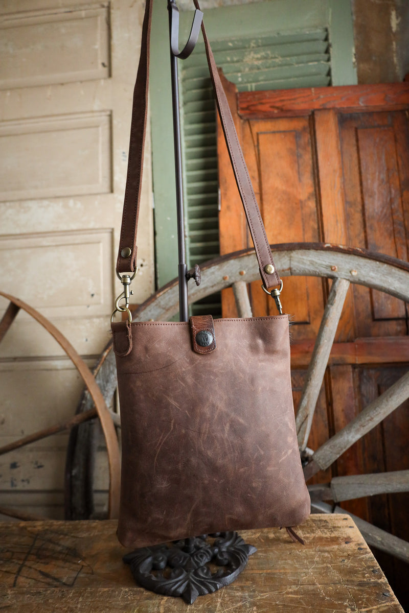 Brown leather tote bag with a strap on a wooden surface with a rustic background