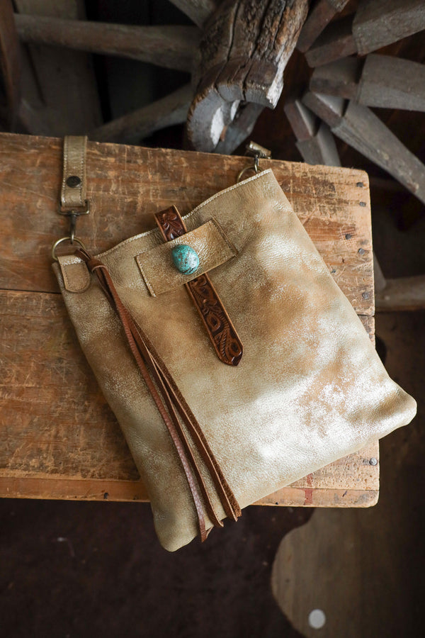 Beige leather pouch with brown strap and turquoise stone on a wooden surface