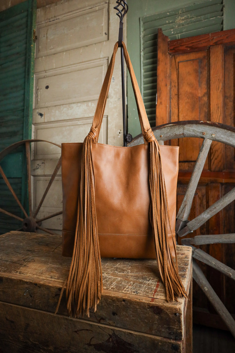 Brown leather bag with fringes on a wooden bench in front of a rustic background