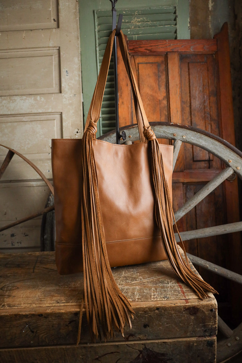 Brown leather tote bag with fringes on a wooden surface with rustic background