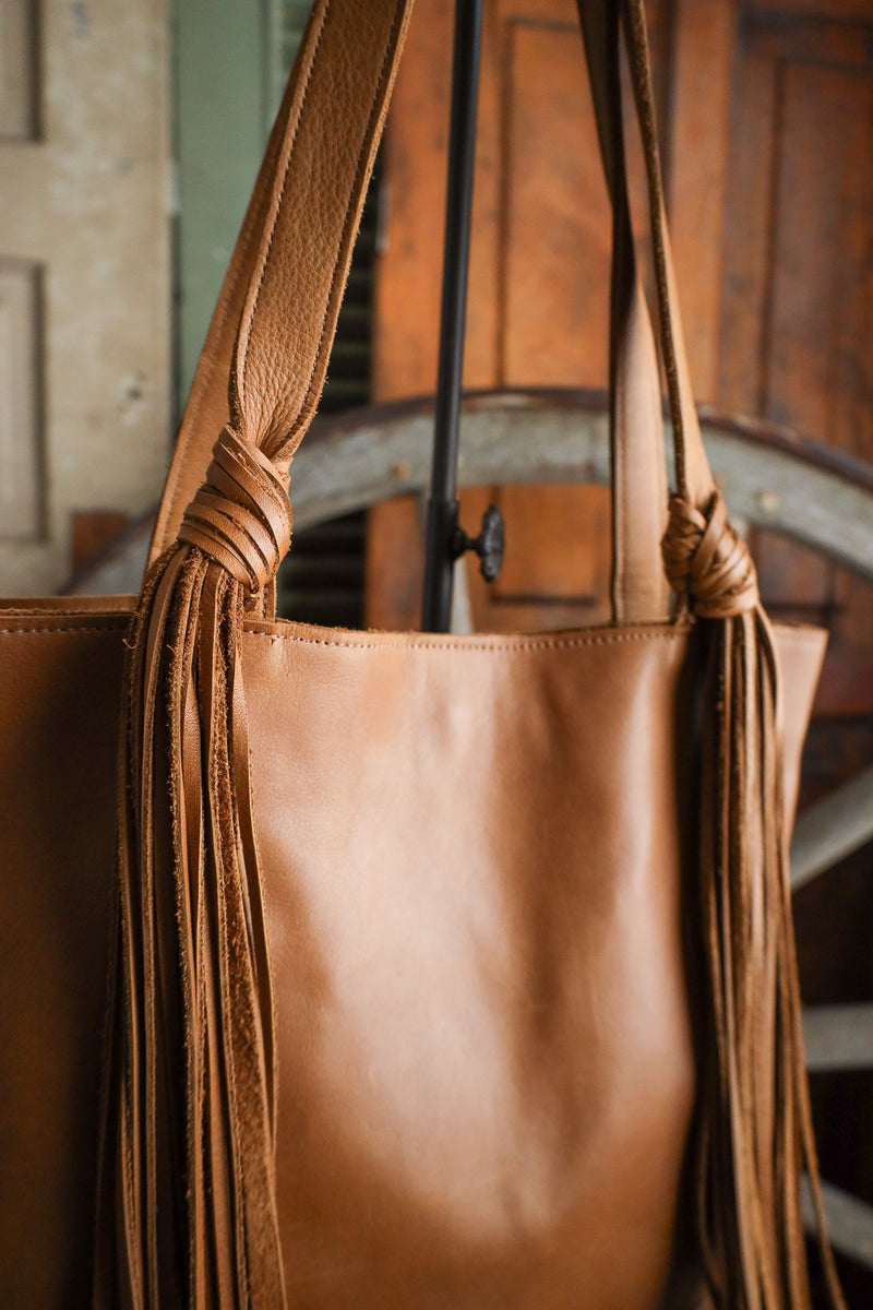 Brown leather tote bag with fringe details in a rustic setting