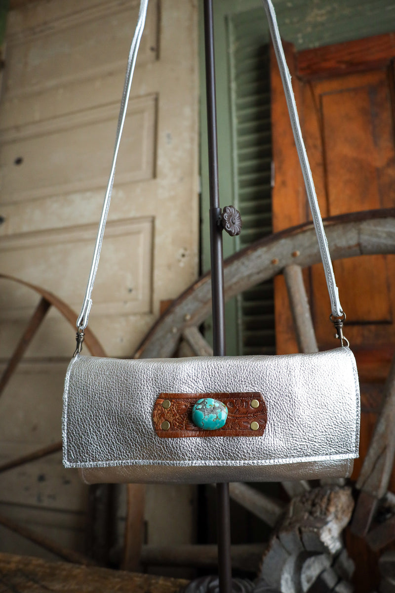 Silver handbag with a brown leather patch and turquoise stone on a rustic background
