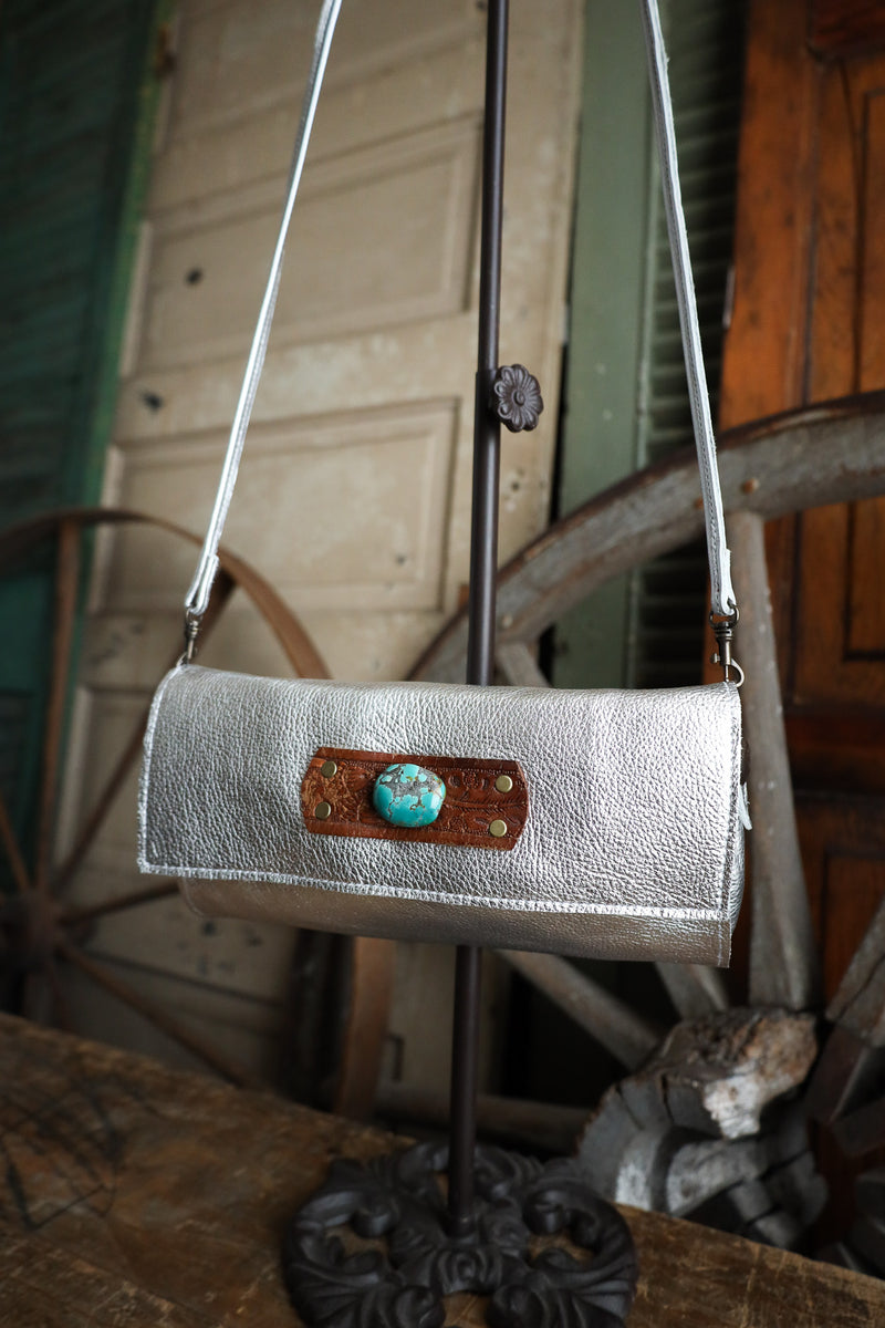 Silver handbag with a turquoise stone clasp on a stand against a rustic background