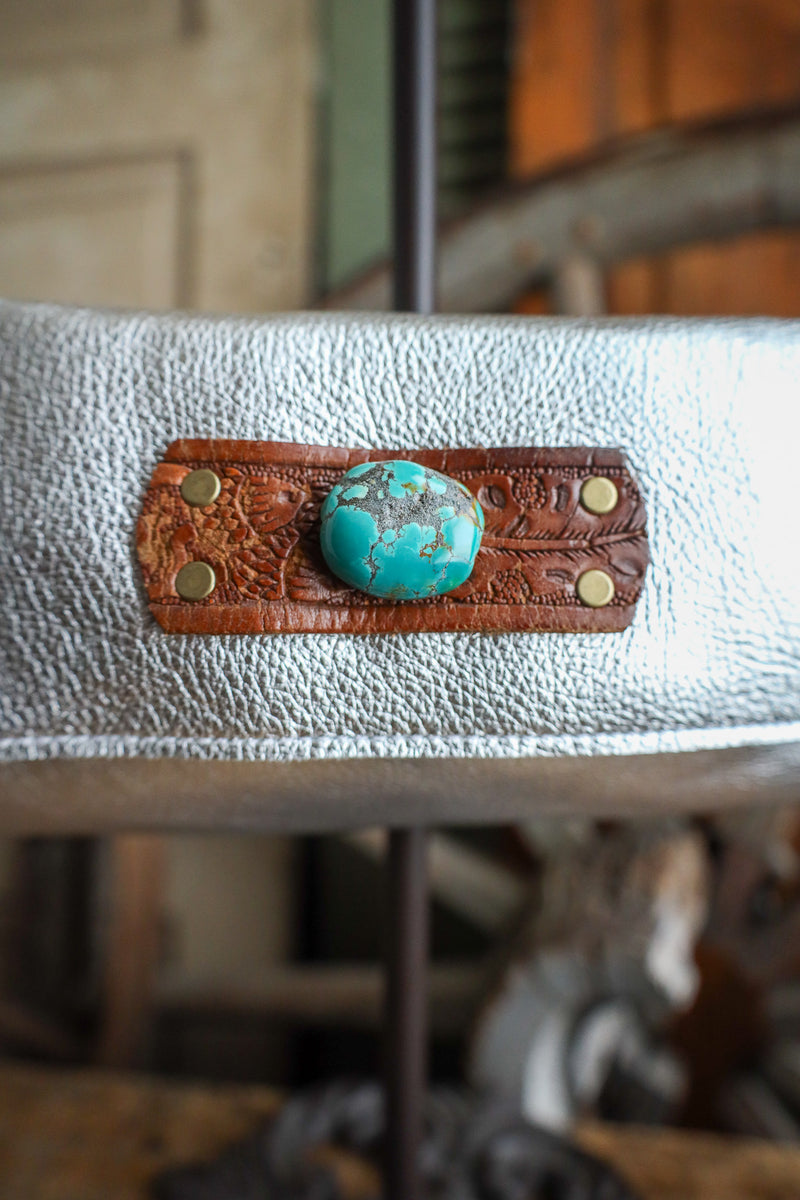 Turquoise stone in a brown leather holder on a white surface with blurred background