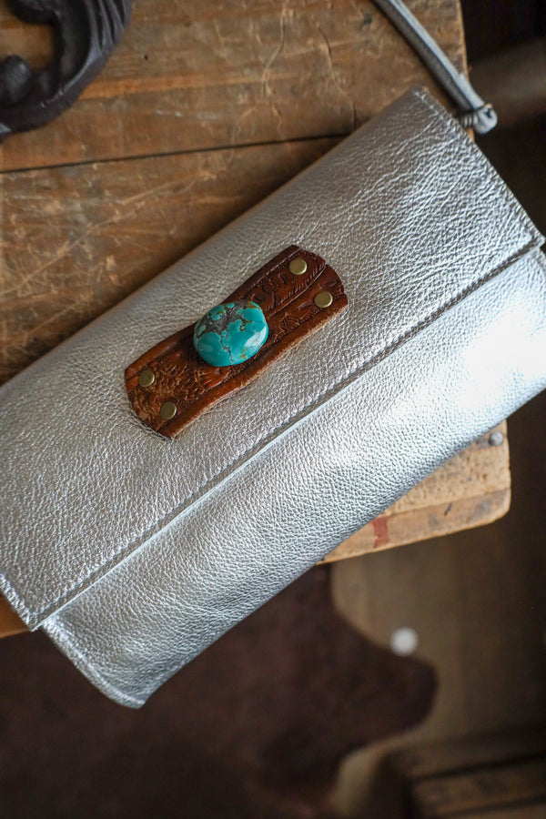 Silver clutch with turquoise stone and brown leather patch on a wooden surface