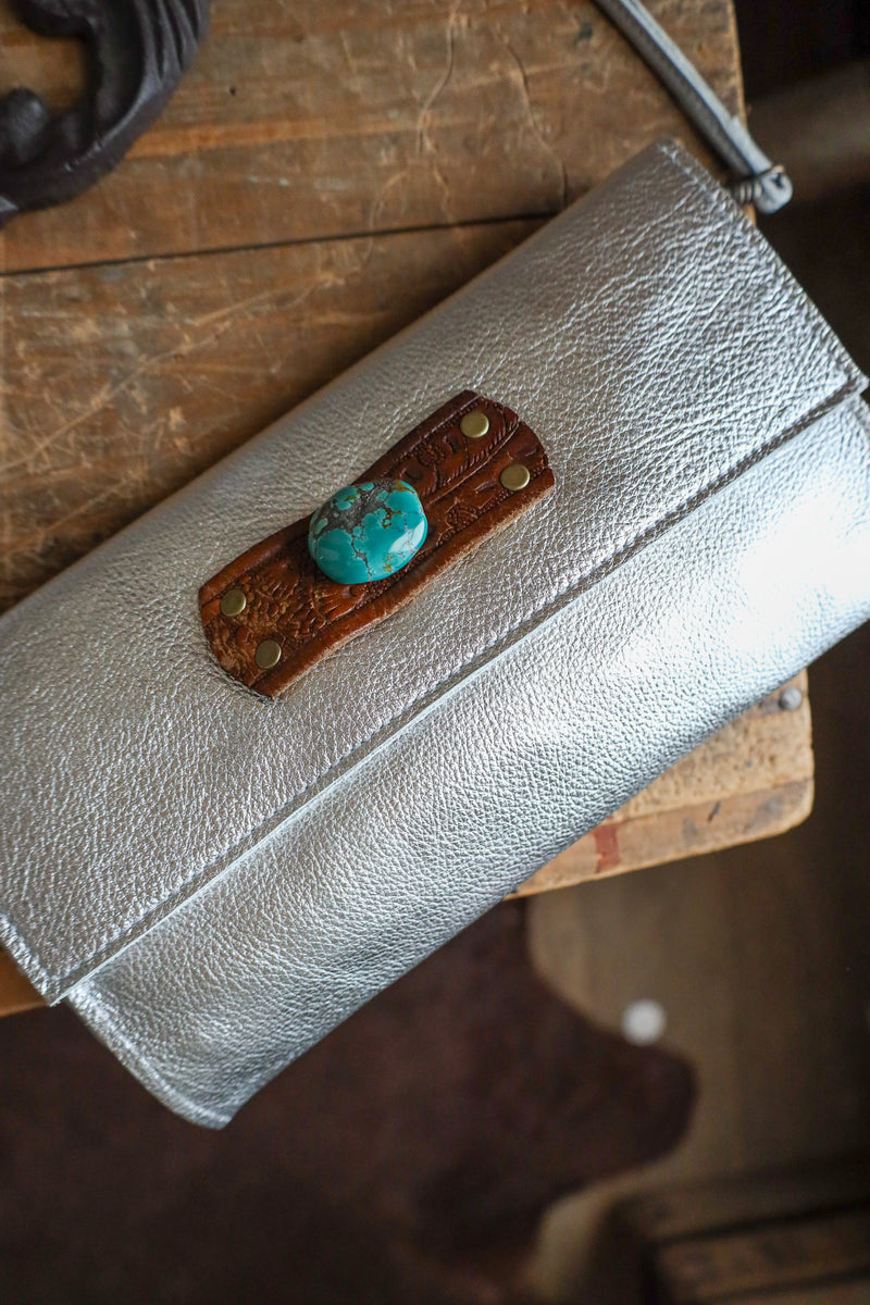 Silver clutch with turquoise stone and brown leather patch on a wooden surface