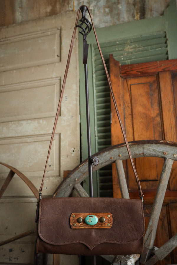 Brown leather handbag with turquoise accents on a rustic background