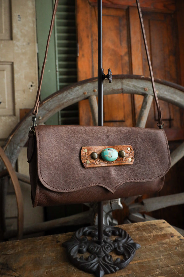 Brown leather handbag with turquoise stones on a metal stand in a rustic setting