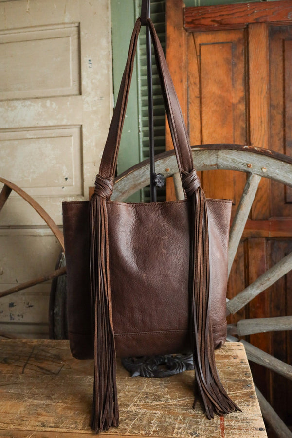 Brown leather tote bag with fringe on a wooden surface with rustic background