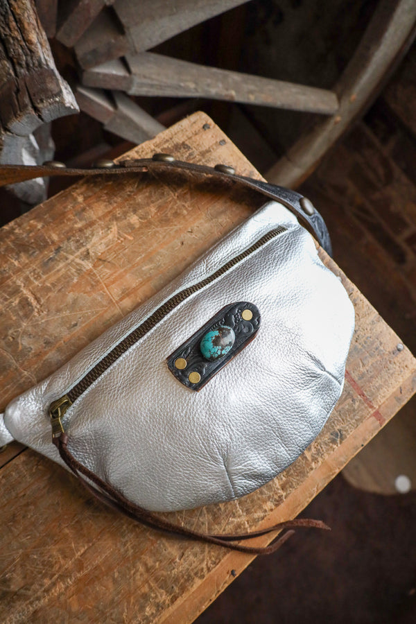 Silver leather bag with a decorative patch on a wooden surface