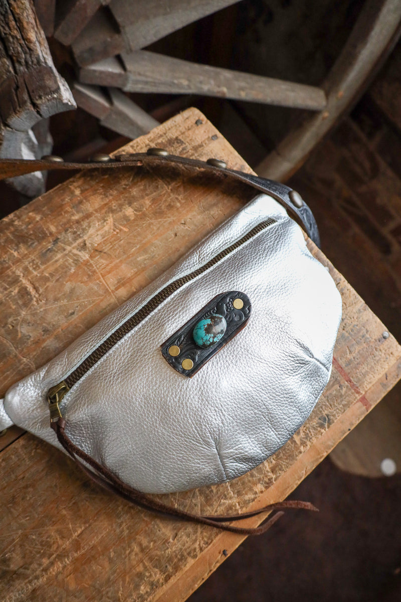 Silver leather bag with a decorative patch on a wooden surface