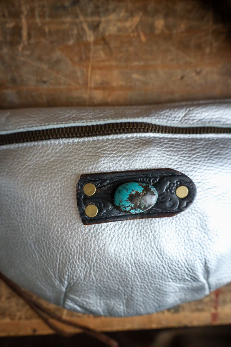 Close-up of a leather pouch with a turquoise stone and gold accents on a wooden surface.