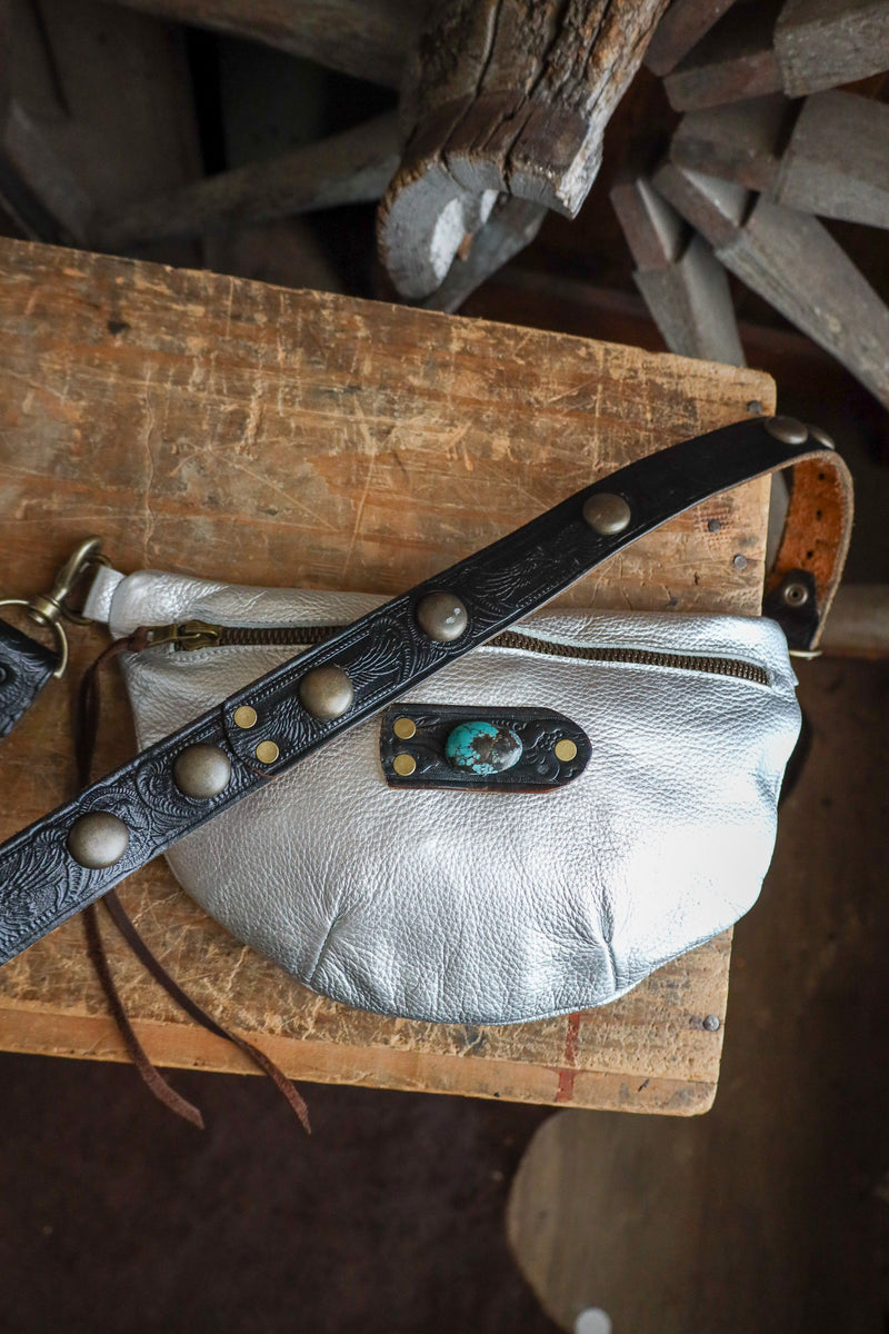 Silver leather bag with black strap on a wooden surface