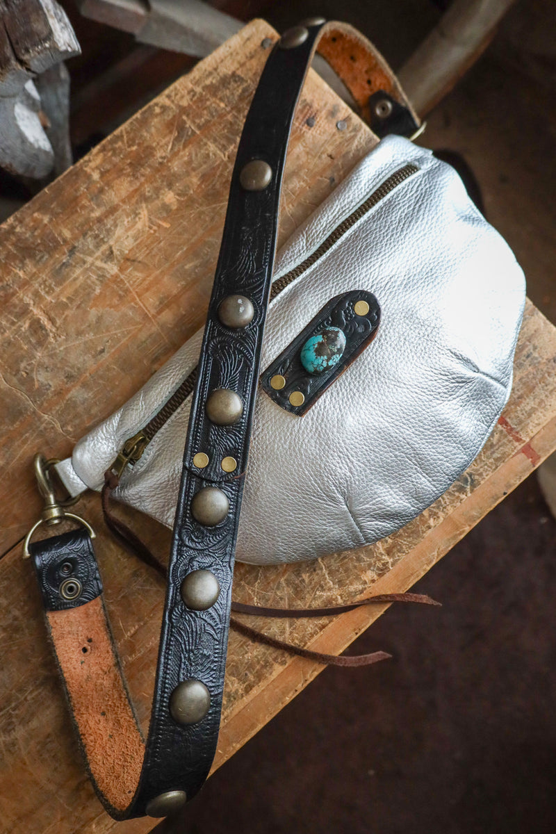 Silver pouch with a black leather strap on a wooden surface