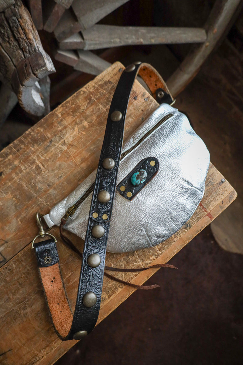 Silver pouch with a black leather strap on a wooden surface