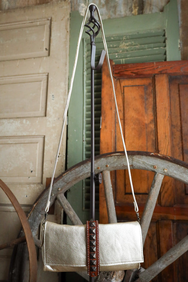 White handbag with brown leather strap and studs hanging on an old wagon wheel.