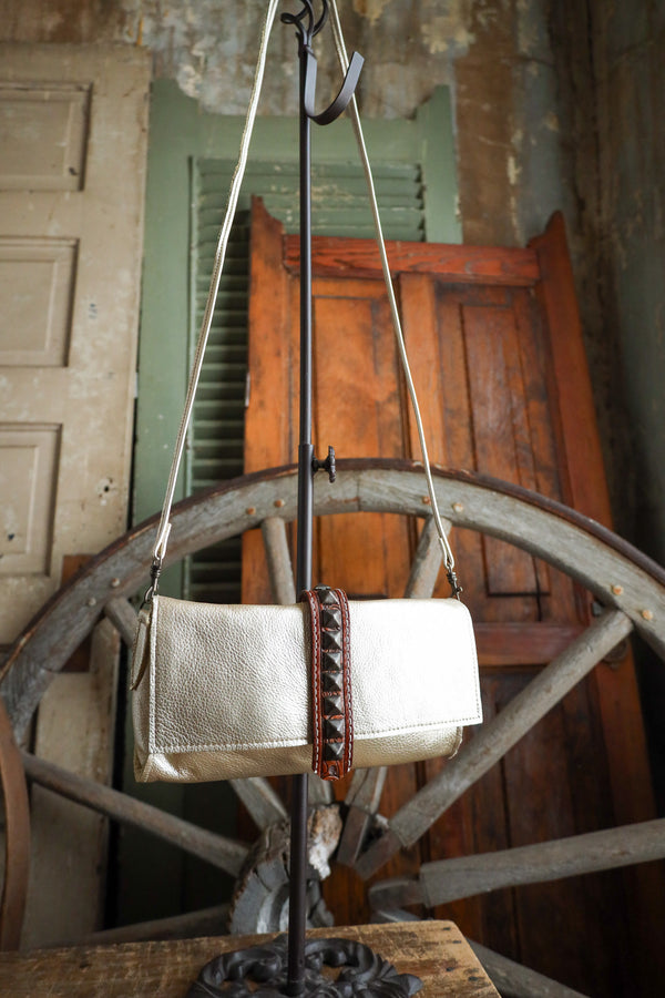White handbag with brown leather strap hanging on a rustic wooden wheel.