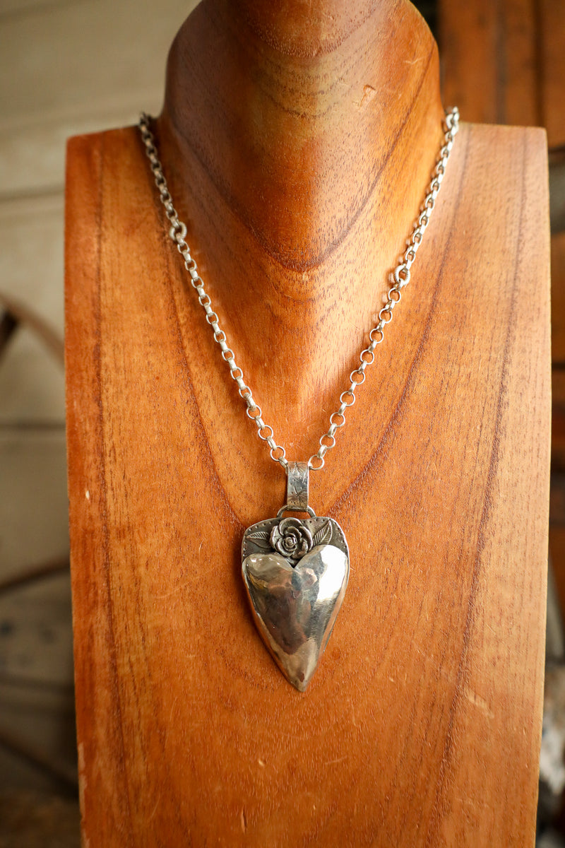 Silver heart-shaped pendant necklace on a wooden mannequin