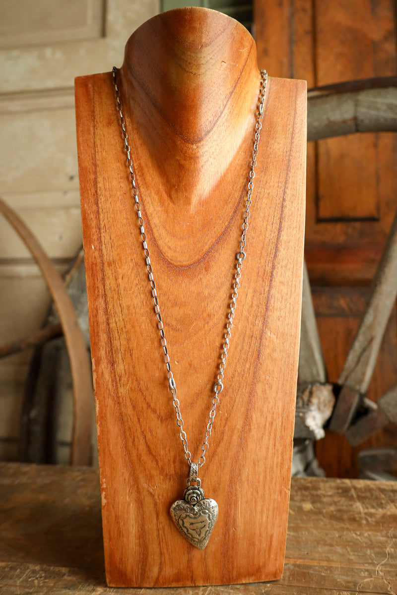 Silver necklace with a heart pendant on a wooden stand.